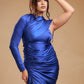 Woman in blue satin one-shoulder ruched dress posing against beige background