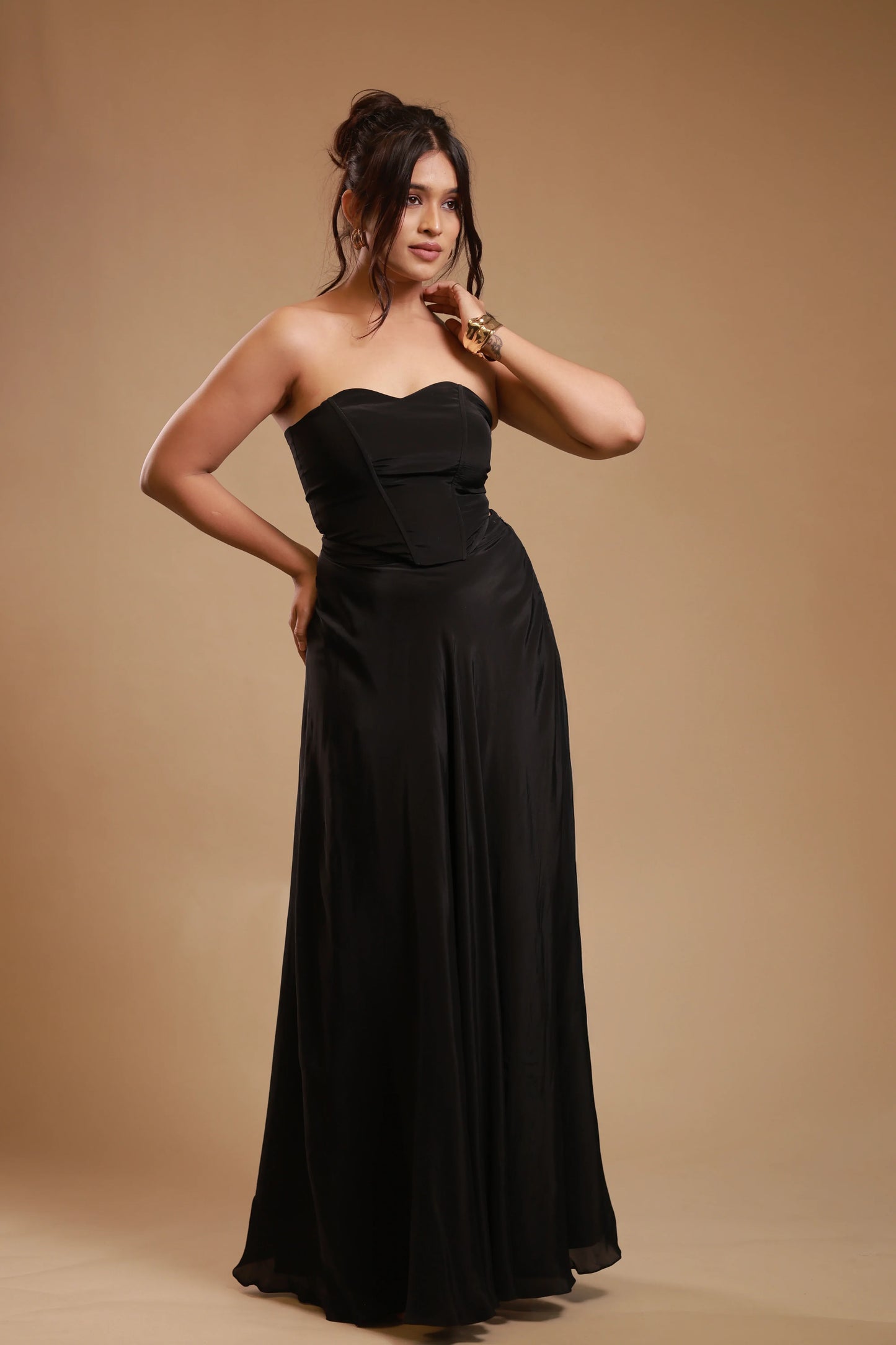 Woman in strapless black satin evening gown posing against beige background