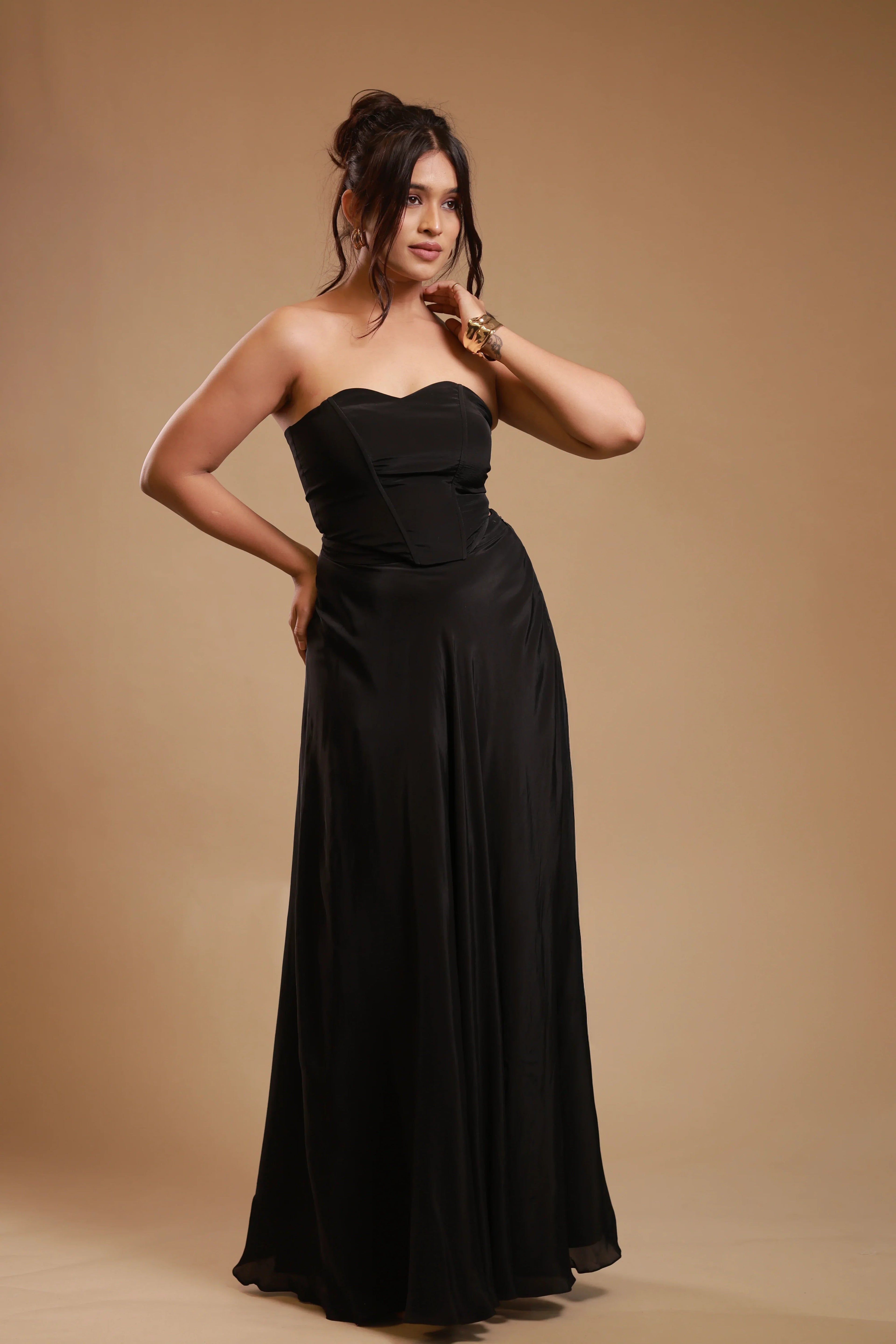 Woman in strapless black satin evening gown posing against beige background
