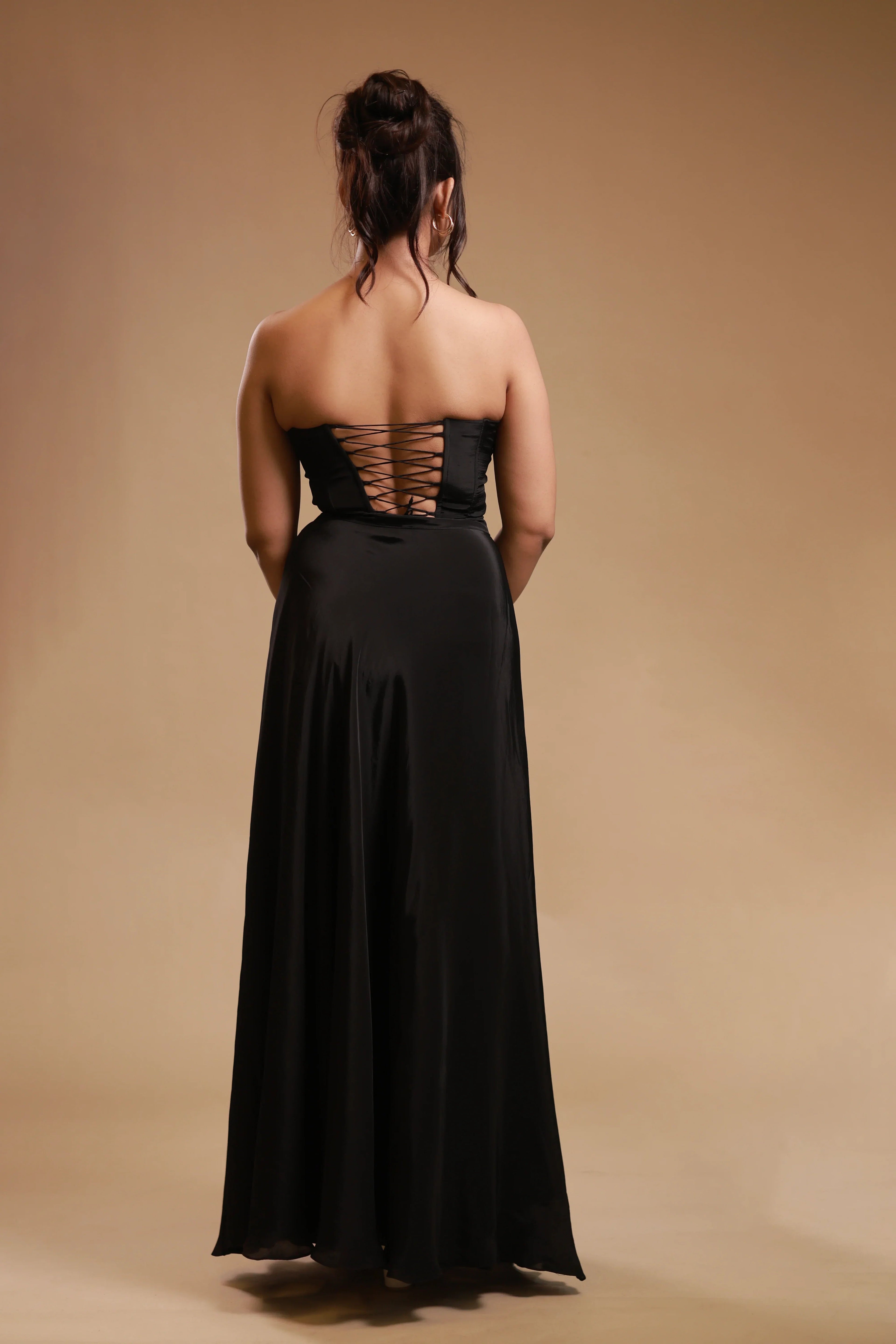 Woman in black strapless evening gown with lace-up back, studio backdrop