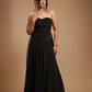 Woman in strapless black satin evening gown with gold bracelet against beige background