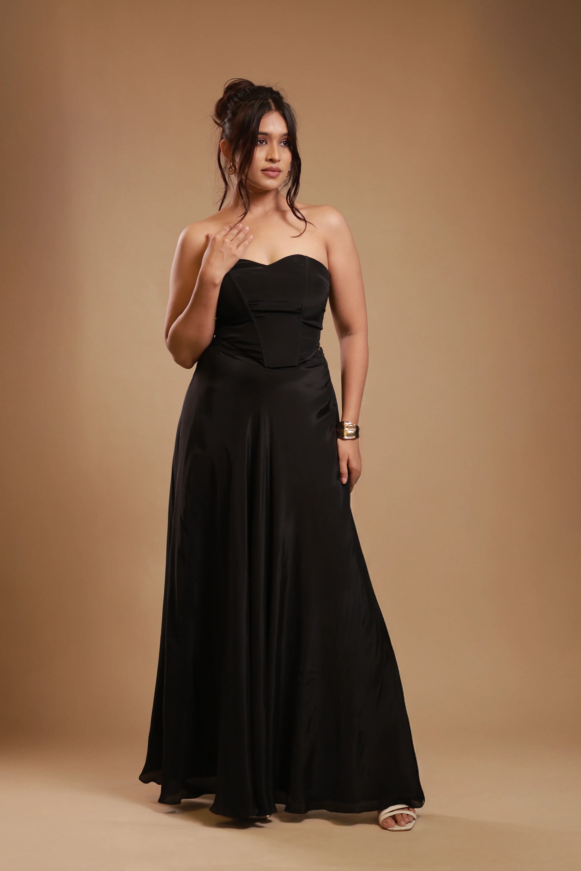 Woman in strapless black satin evening gown with gold bracelet against beige background