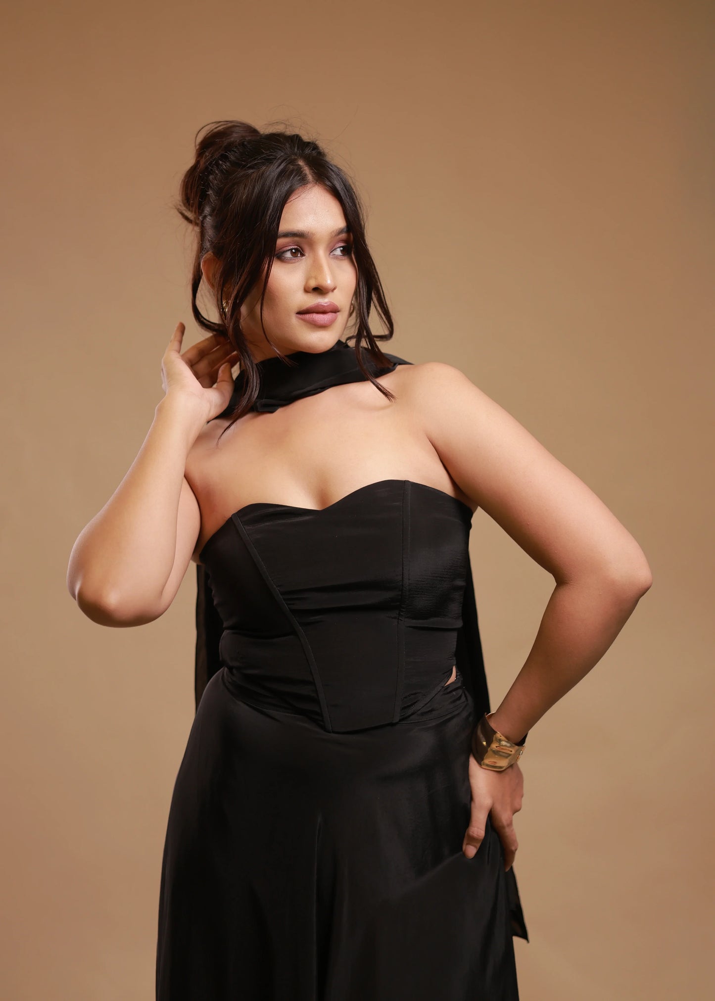 Woman in black strapless satin dress with scarf, gold bracelet, neutral studio background