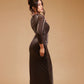 Woman in shimmering black evening gown with long sleeves, posing against beige background