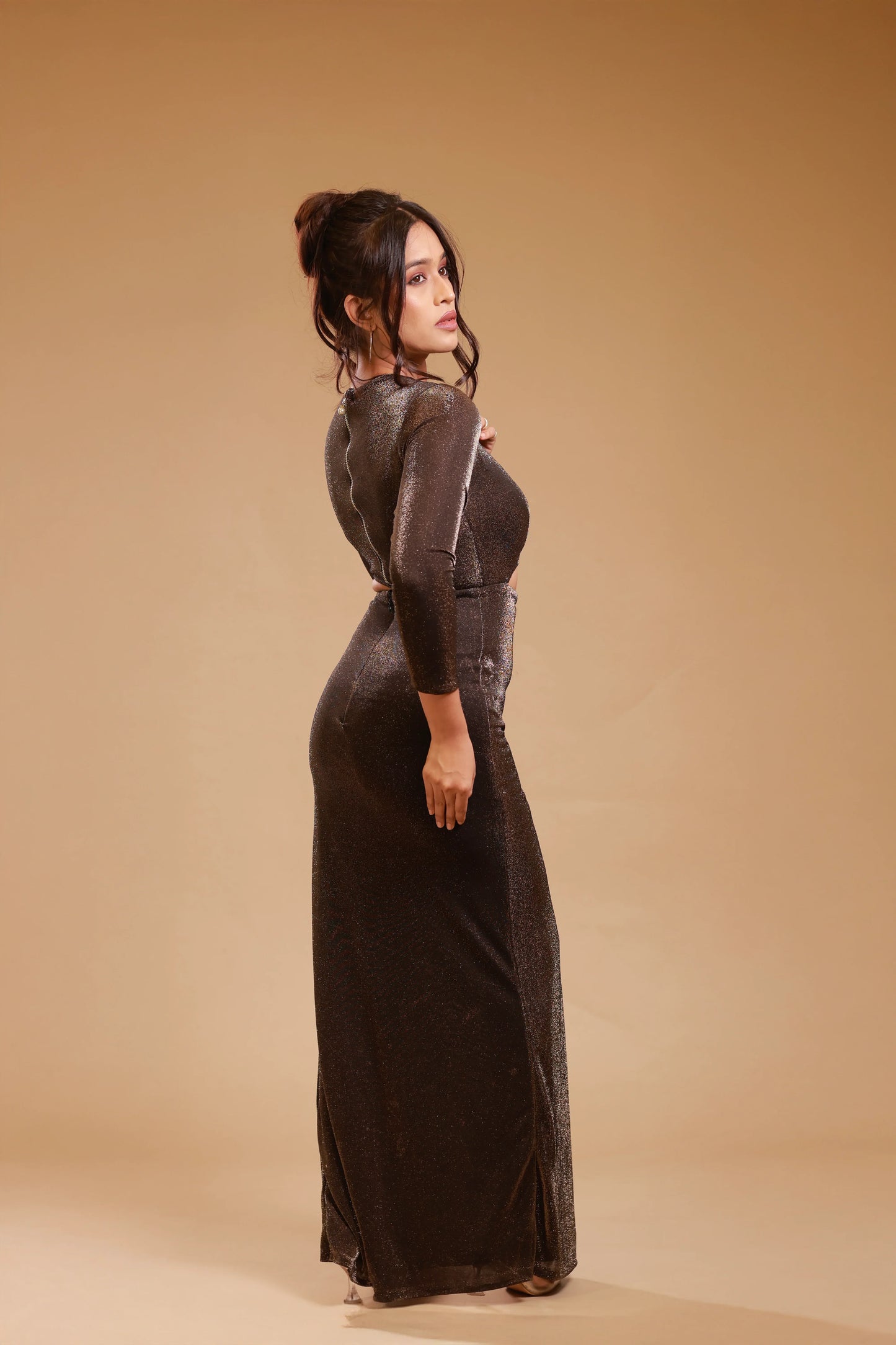Woman in shimmering black evening gown with long sleeves, posing against beige background