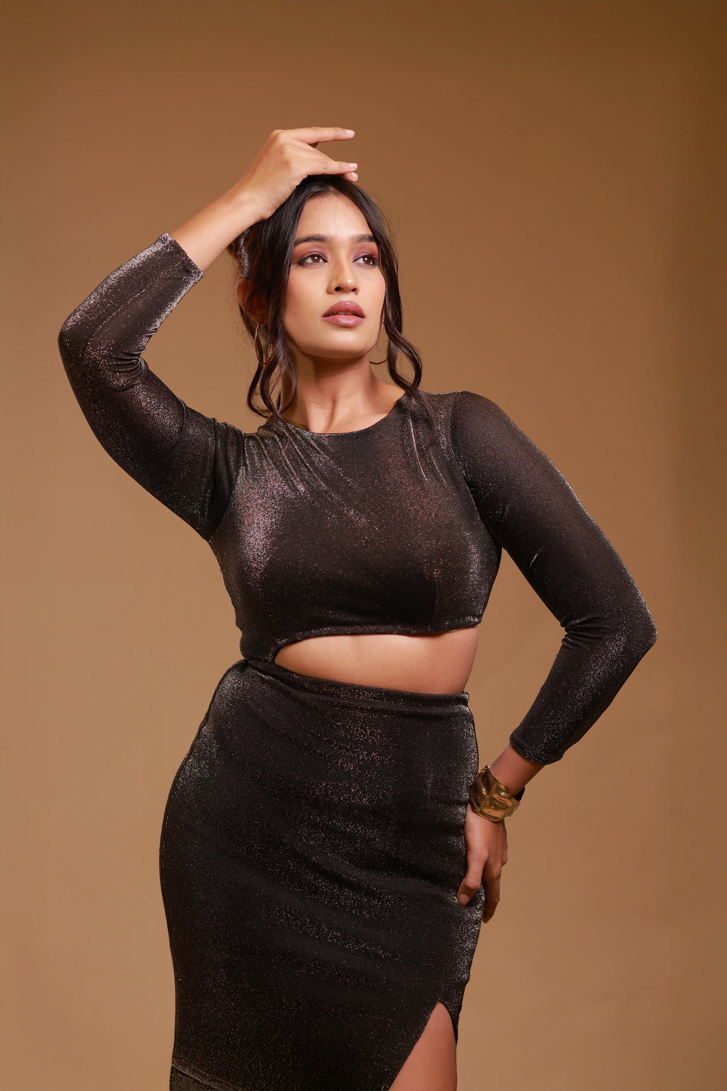 Woman modeling black shimmer cutout dress with long sleeves on a beige background