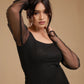 Woman in black mesh sleeve dress posing against beige background