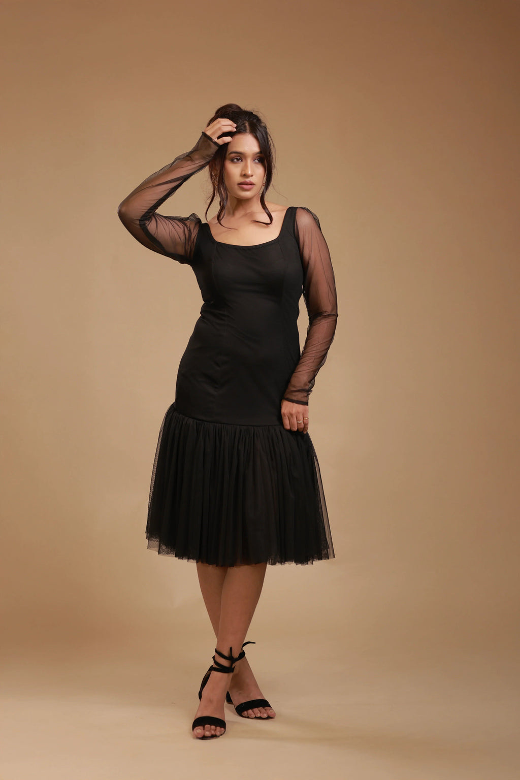 Woman wearing black mesh long sleeve dress with tulle skirt, posing on beige studio background