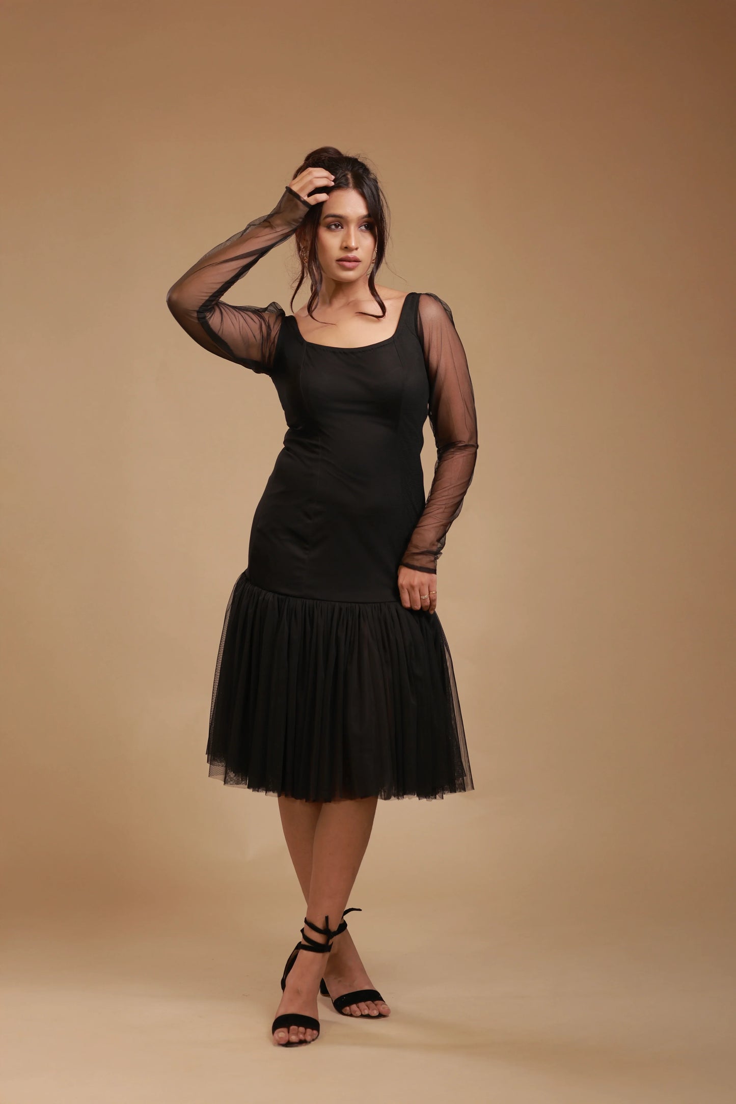 Woman wearing black mesh long sleeve dress with tulle skirt, posing on beige studio background