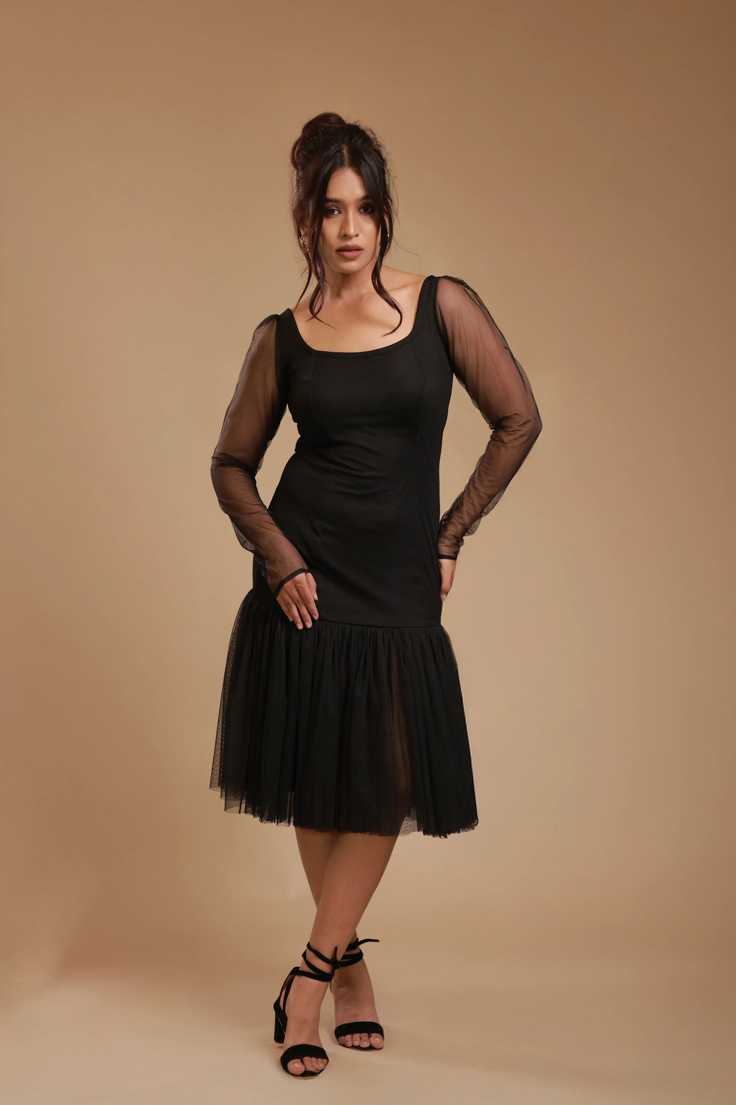 Woman modeling black mesh sleeve dress with tulle skirt and ankle strap heels in studio